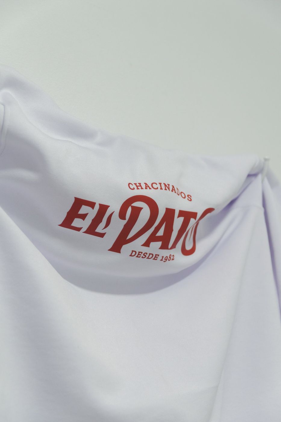 Detalle del logo rojo de Chacinados El Pato en un buzo blanco